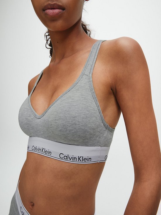 Model in grijze Calvin Klein bralette met V-hals en wit logo-elastiek.