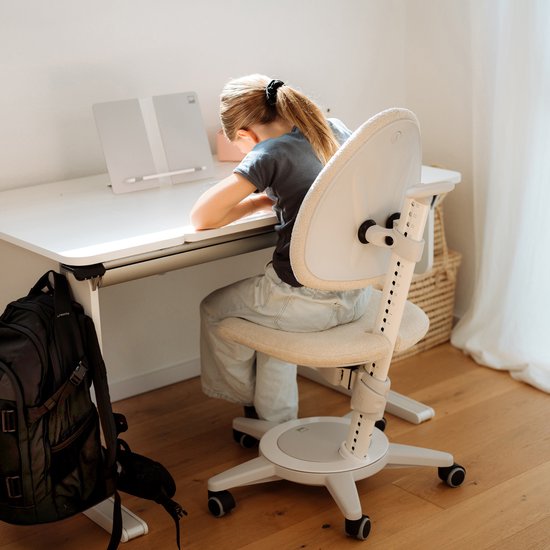 Meisje met paardenstaart zit aan een bureau, een verstelbare stoel met stoffen rugleuning en zitting.