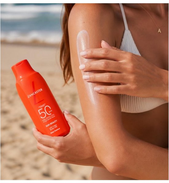 Een vrouw met een witte bikini brengt Lancaster Sun Beauty Body Milk SPF50 aan op haar arm.