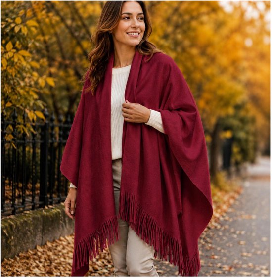 Vrouw in een witte trui en beige broek draagt een bordeauxrode omslagdoek met franjes.