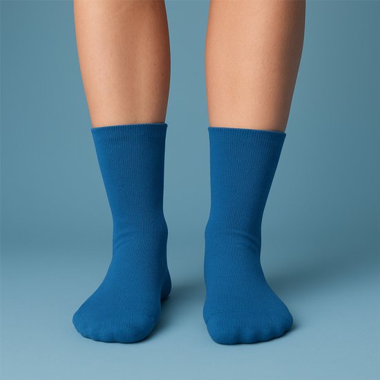 Voeten in effen blauwe sokken met een fijne ribbelboord, op een blauwe achtergrond.