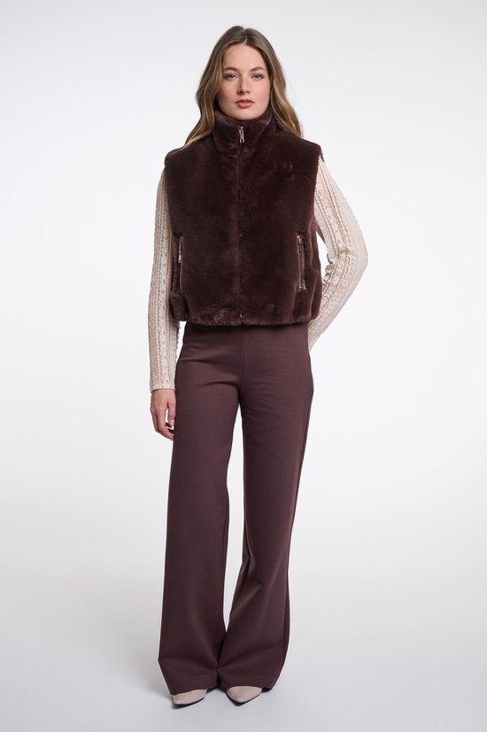Model in bruin imitatiebont gilet, beige top met kant en wijde bruine broek.