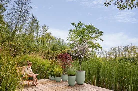 Buitenopstelling met een vrouw op een bankje, diverse lichtgroene Elho Sereh potten met planten.