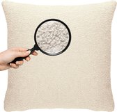 Een hand met vergrootglas toont de fijne textuur van een crème-kleurig teddy kussen.