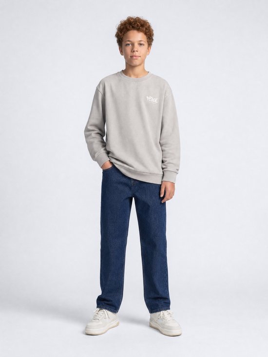 Jongen met grijze sweater met witte 'Petrol' logo, blauwe jeans en witte sneakers.