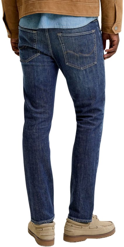 Man in een spijkerbroek, bruine jas en blauw overhemd, van achteren gezien.