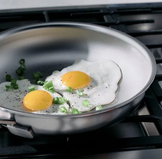 Twee gebakken eieren met lente-ui in een zilverkleurige pan op een gasfornuis.