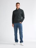 Man met donkergroen vest met rits, hoge kraag en jeans.