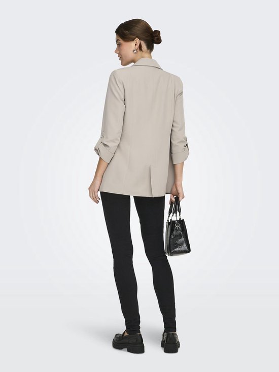 Model met beige blazer, zwarte skinny jeans en instappers, van achteren gezien.
