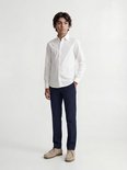 Garçon en chemise blanche à manches longues et pantalon bleu marine, debout.