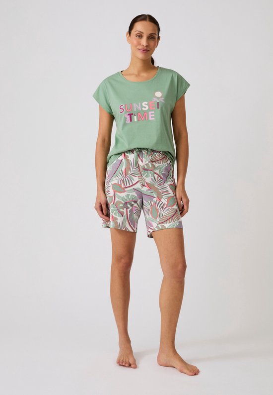 Model in een lichtgroen T-shirt met "SUNSET TIME" print en een short met tropische bladerenprint.