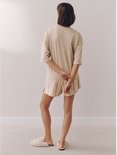 Model in een beige oversized T-shirt en een gestreepte short, staand met de rug naar de camera. Beige en witte strepen op de short.