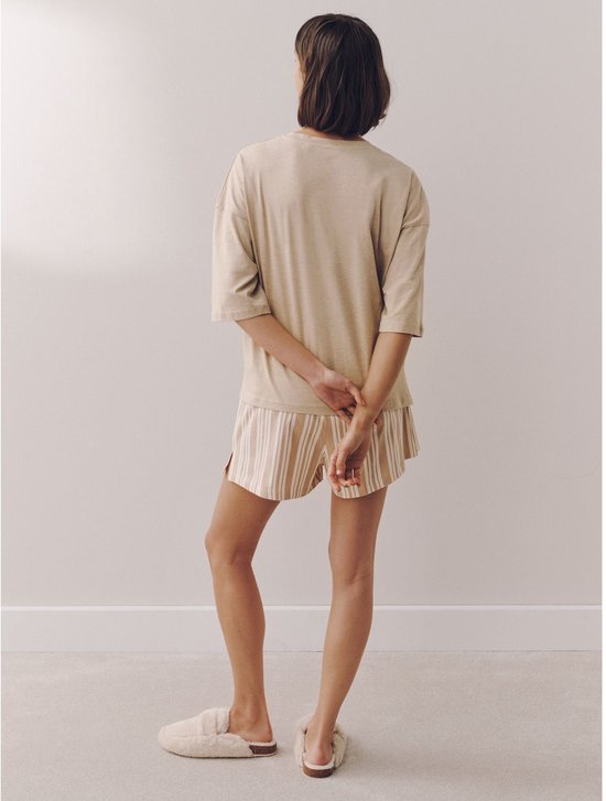 Model in een beige oversized T-shirt en een gestreepte short, staand met de rug naar de camera. Beige en witte strepen op de short.