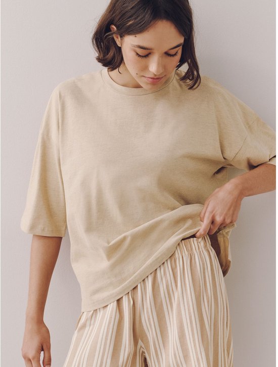 Model draagt een beige pyjamaset. De top is effen en de short heeft verticale strepen.
