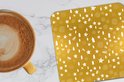 Sous-verre doré à motif de Noël blanc à côté d'une tasse de café.