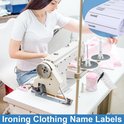 Een vrouw naait met een naaimachine. Op tafel liggen een rol met naamlabels, een pen en een speldkussen. De tekst "Ironing Clothing Name Labels" is zichtbaar.