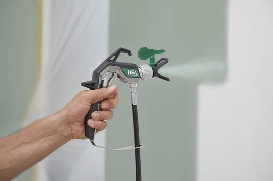 Hand houdt een zwarte Wagner HEA verfspuit vast die verf spuit op een muur.