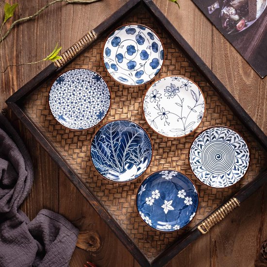 Zes ronde, blauw-witte keramische schaaltjes met diverse patronen zoals bloemen, bladeren en spiralen, gerangschikt in een mand.