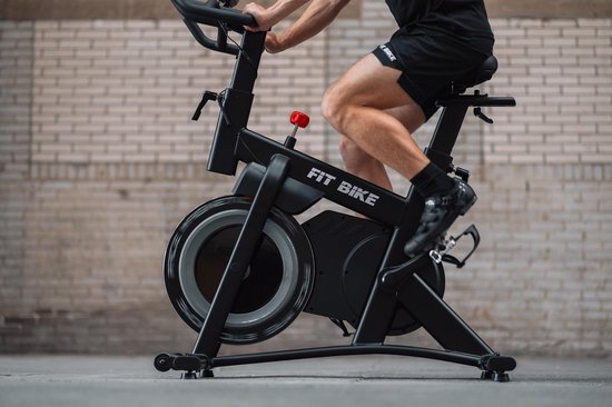 Dichtbij opname van een zwarte spinfiets met een man die erop fietst. De rode weerstandsknop is zichtbaar.