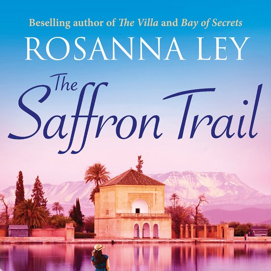 Couverture du livre 'The Saffron Trail' avec une femme au premier plan regardant un bâtiment avec un lac et des montagnes en arrière-plan.