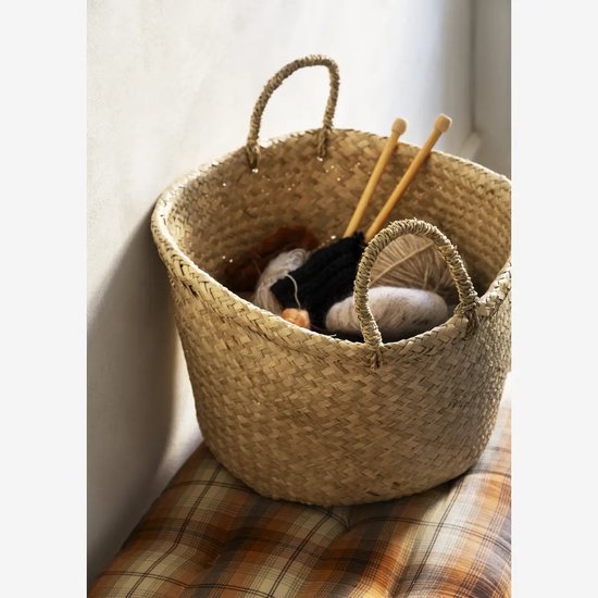 Gevlochten mand met touwhandvatten, gevuld met bruin, zwart en wit garen en breinaalden.