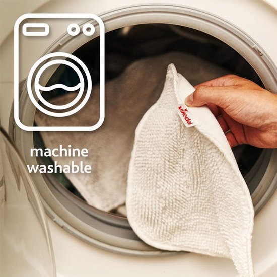 Hand stopt een wit Vileda microvezel opzetstuk in een wasmachine.