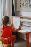Kind met vlecht zit aan tafel en houdt roze lichttablet met getekende prinses.