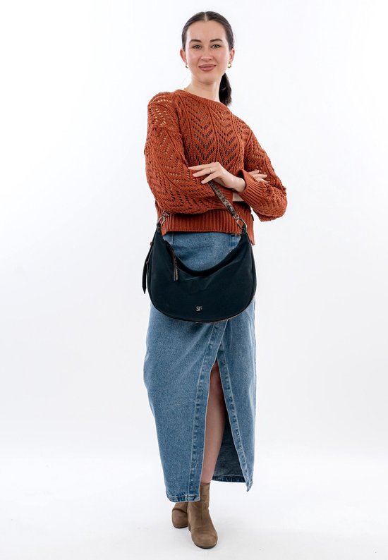 Model met gekruiste armen, draagt een donkerblauwe buideltas met dierenprint accenten, spijkerrok en oranje gebreide trui.