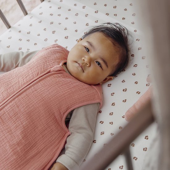 Baby in een roze mousseline slaapzak met panterprint bedje.