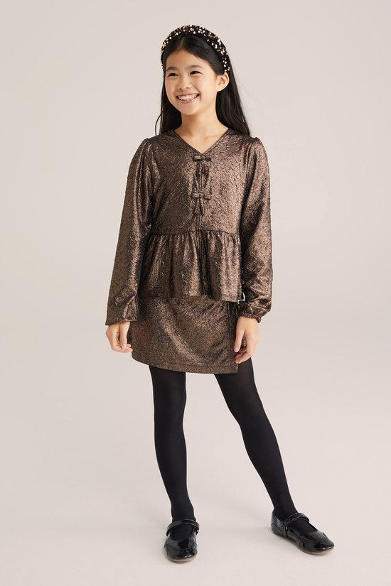 Meisje in bruin metallic peplum T-shirt met strikdetail en zwarte panty.