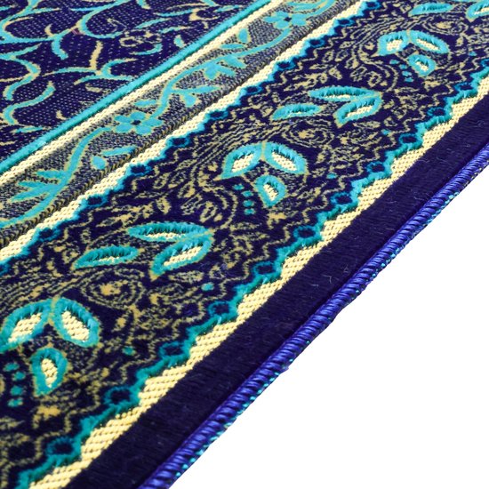 Gros plan d'un tapis de prière bleu foncé avec des motifs de feuilles bleus et dorés, avec une bordure jaune et des franges bleues.