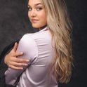 Model met blond haar, draagt een lichtroze satijnen pyjama met zwarte biezen. Ze kijkt over haar schouder.