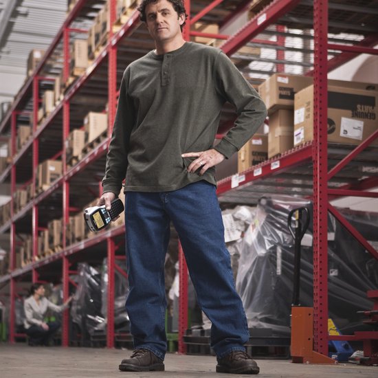 Een man met een donkergroene longsleeve en spijkerbroek staat in een magazijn en houdt een Dymo labelmaker vast.