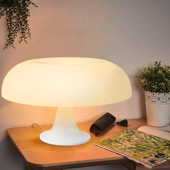 Lampe de table blanche champignon sur une table d'appoint en bois, éclairée d'une lumière chaude, avec une plante et un magazine à côté.