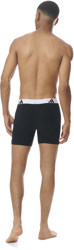 Man van achteren gezien, met zwarte boxershorts met brede, witte Adidas-band met logo's.