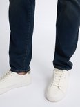 Onderkant van een man in spijkerbroek en witte sneakers.