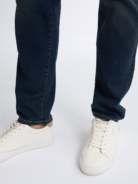 Onderkant van een man in spijkerbroek en witte sneakers.