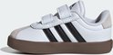 Zijaanzicht van een witte sneaker met zwarte strepen, klittenbandsluiting en bruine zool.