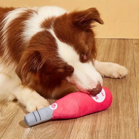 Un chien brun et blanc joue avec une peluche rose en forme de bouteille étiquetée "SPARKLING ROSE".