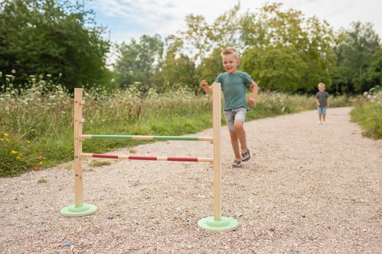 Jongen rent naar een hordenparcours met twee staanders en twee balken: groen-hout en rood-wit geblokt.