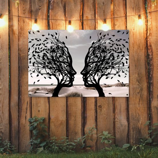 Zwart silhouet van twee bomen met gezichtsprofielen die naar elkaar toe staan, boven tuinverlichting.