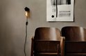 Edison-stijl lamp met gouden gloed aan een zwart snoer aan een muur naast twee houten stoelen en een abstract schilderij.