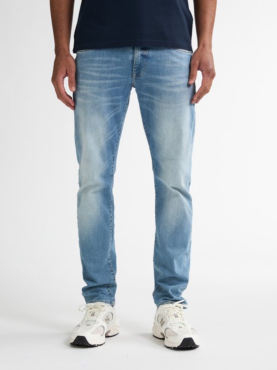 Man draagt een marineblauwe polo en een lichtblauwe slim fit jeans met lichte wassing.