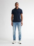Man draagt een marineblauwe polo en lichtblauwe slim fit jeans met witte sneakers.