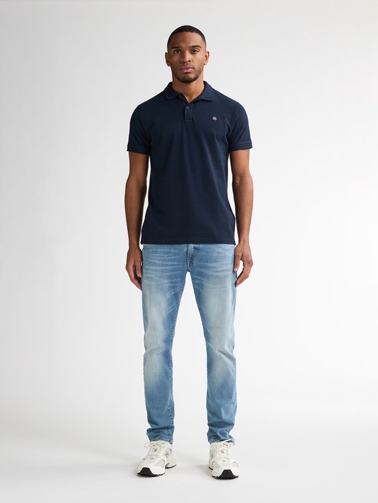 Man draagt een marineblauwe polo en lichtblauwe slim fit jeans met witte sneakers.