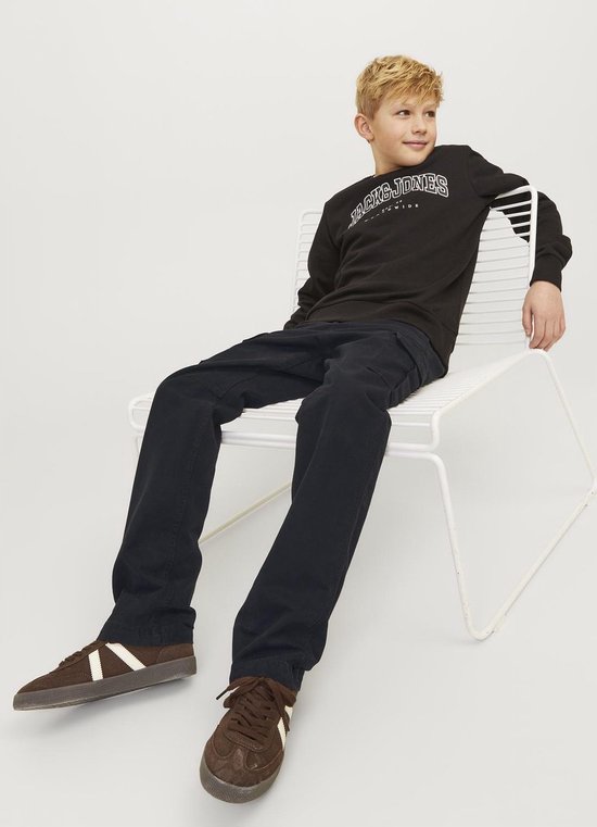 Jongen in donkerblauwe cargobroek en zwart Jack & Jones sweatshirt, zittend op een stoel.