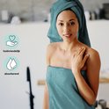 Une femme avec une serviette sur la tête et une autour de son corps. Elle sourit et touche son épaule. À gauche, des icônes pour doux pour la peau et absorbant.