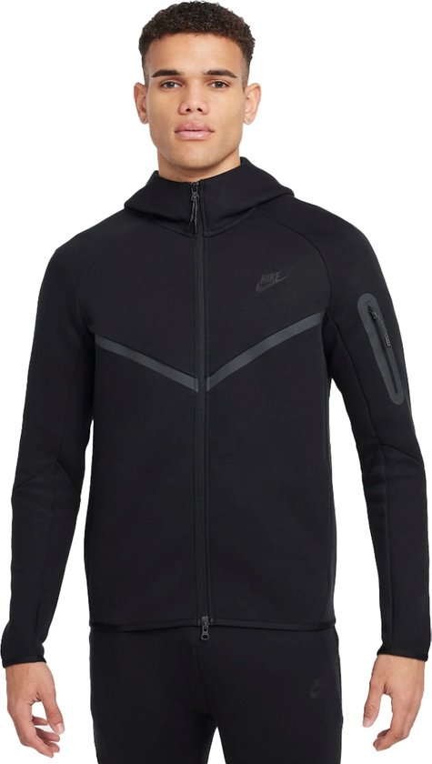 Man in het zwart gekleed in een Nike Tech Fleece hoodie met rits, en broek.