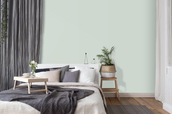 Slaapkamer met een bed met saliegroene muur, grijze gordijnen en houten vloer.