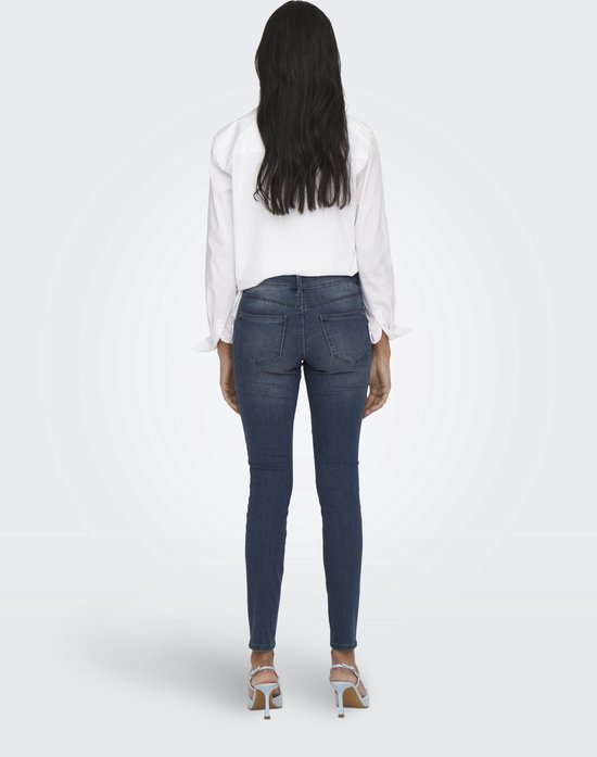 Model van achteren in een donkerblauwe skinny jeans en witte blouse.